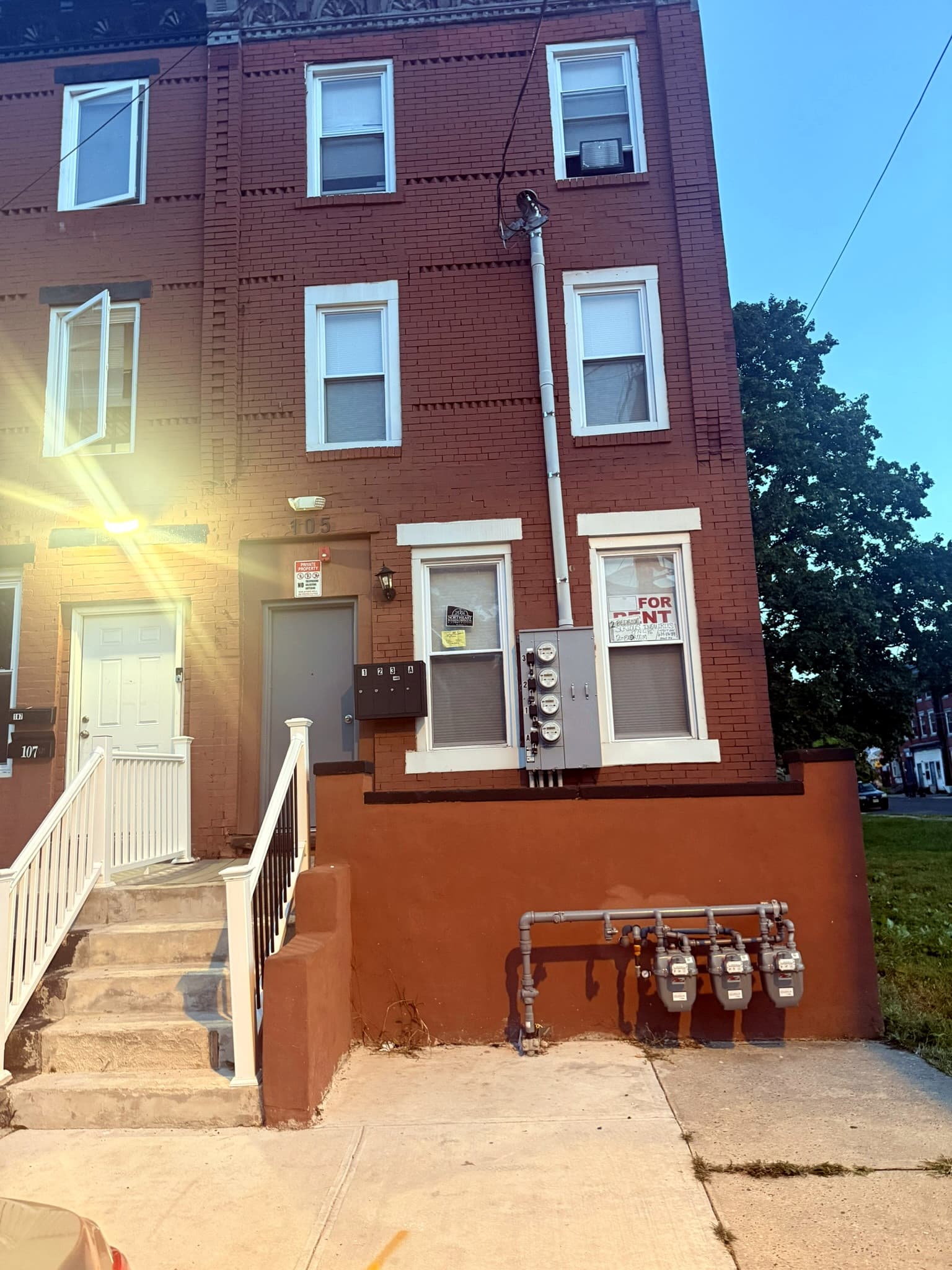 Brick residence at dusk, with a for-rent sign in a first-floor window.