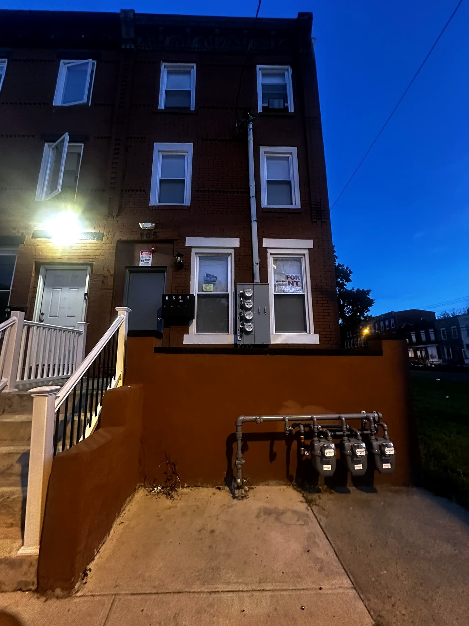 The same brick residence after dark, with front steps and utility meters.