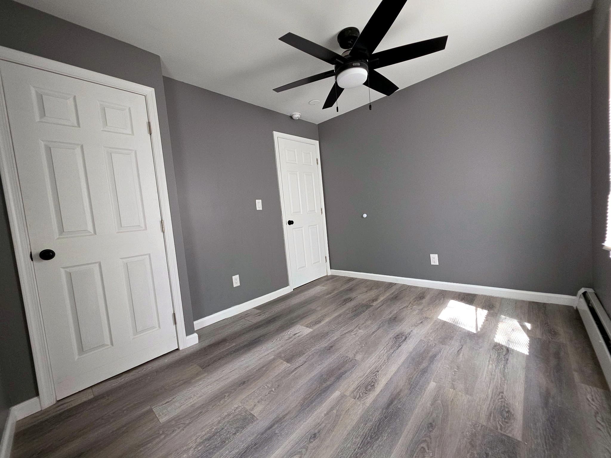 Empty room with two white doors, gray walls, and a ceiling fan.