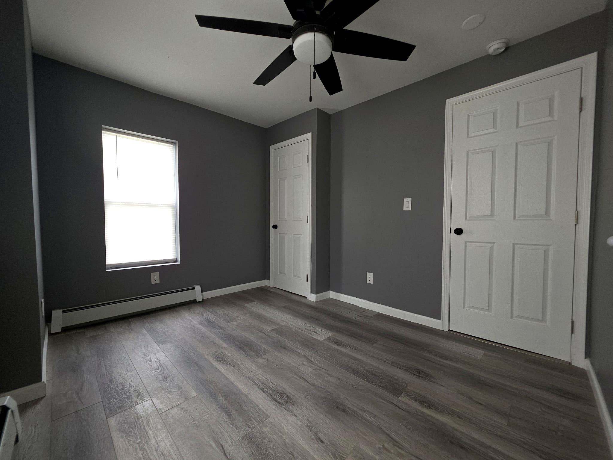 Empty room with one window, two white doors, and a ceiling fan.